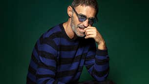 A man in sunglasses with one hand up to his mouth