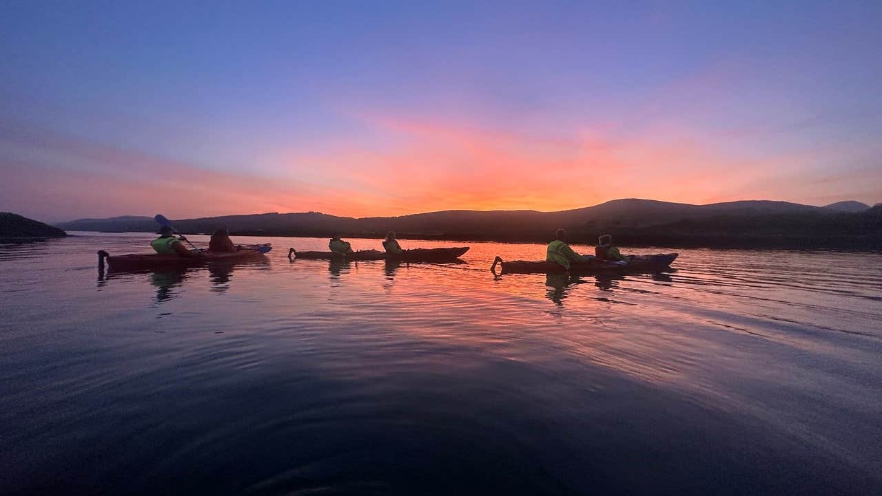 A group of kayakers on Kenmare Bay with a colourful sunset