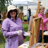 Easels set up outdoors with smiling woman in a hat painting