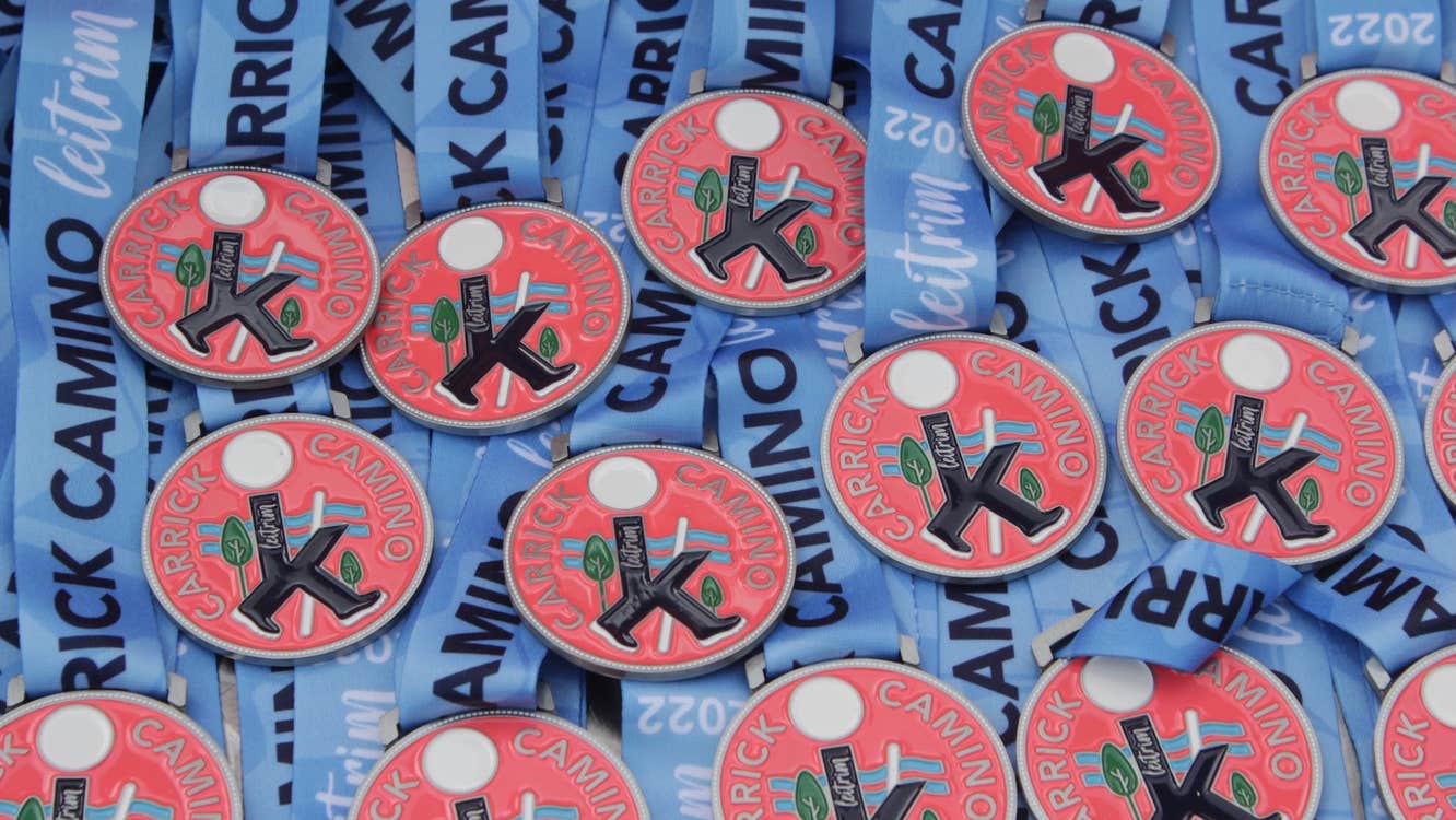 Lots of round red medals with logo for Carrick Camino on and blue ribbons