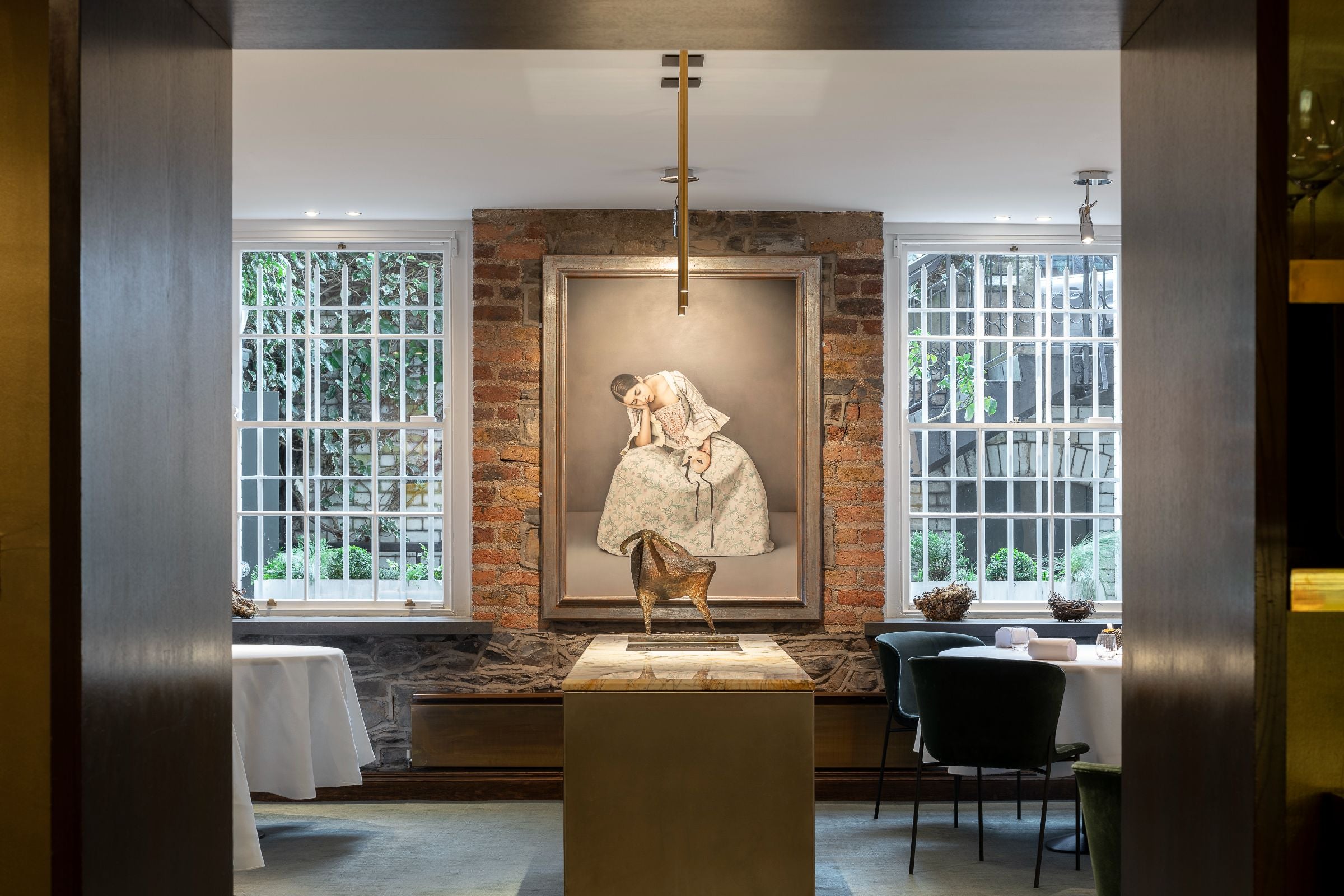 Interior shot of Chapter One with exposed brick wall and a painting of a woman. Tables with white linen and black velvet chairs around them.