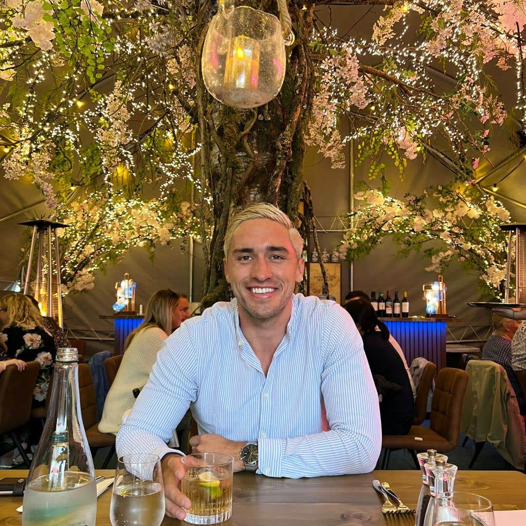 Man smiling at the camera with a big tree behind him in a restaurant with fairy lights hung from the branches.