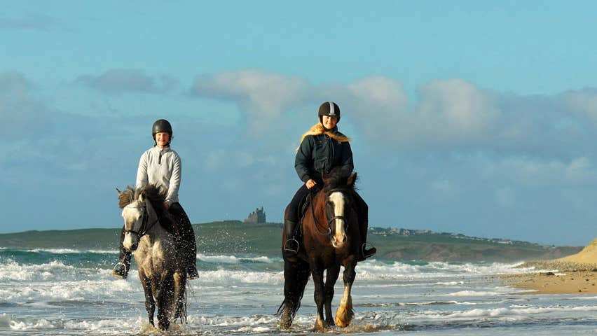 Two horse riders in the surf on the beach castle in the background