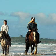 Two horse riders in the surf on the beach castle in the background