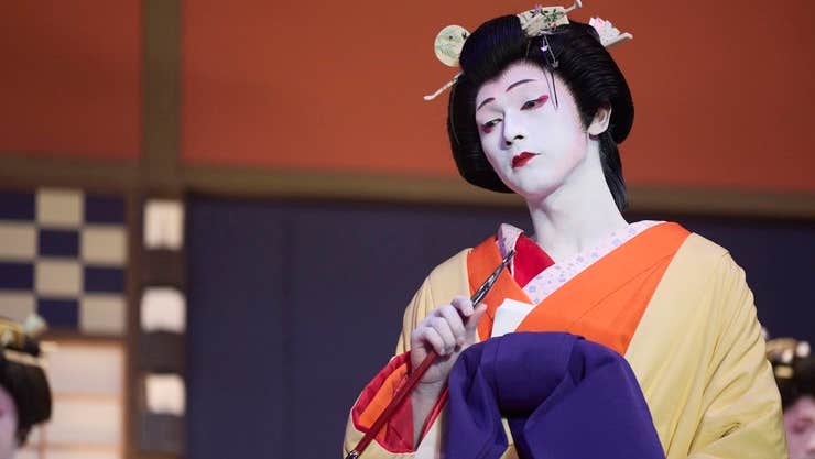 A sad person with very white painted face and black hair tied up in Japanese costume