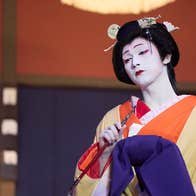 A sad person with very white painted face and black hair tied up in Japanese costume