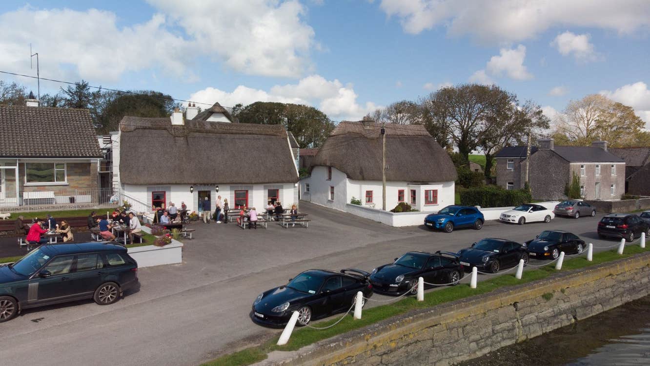 The exterior of a thatched cottage with people sitting outside