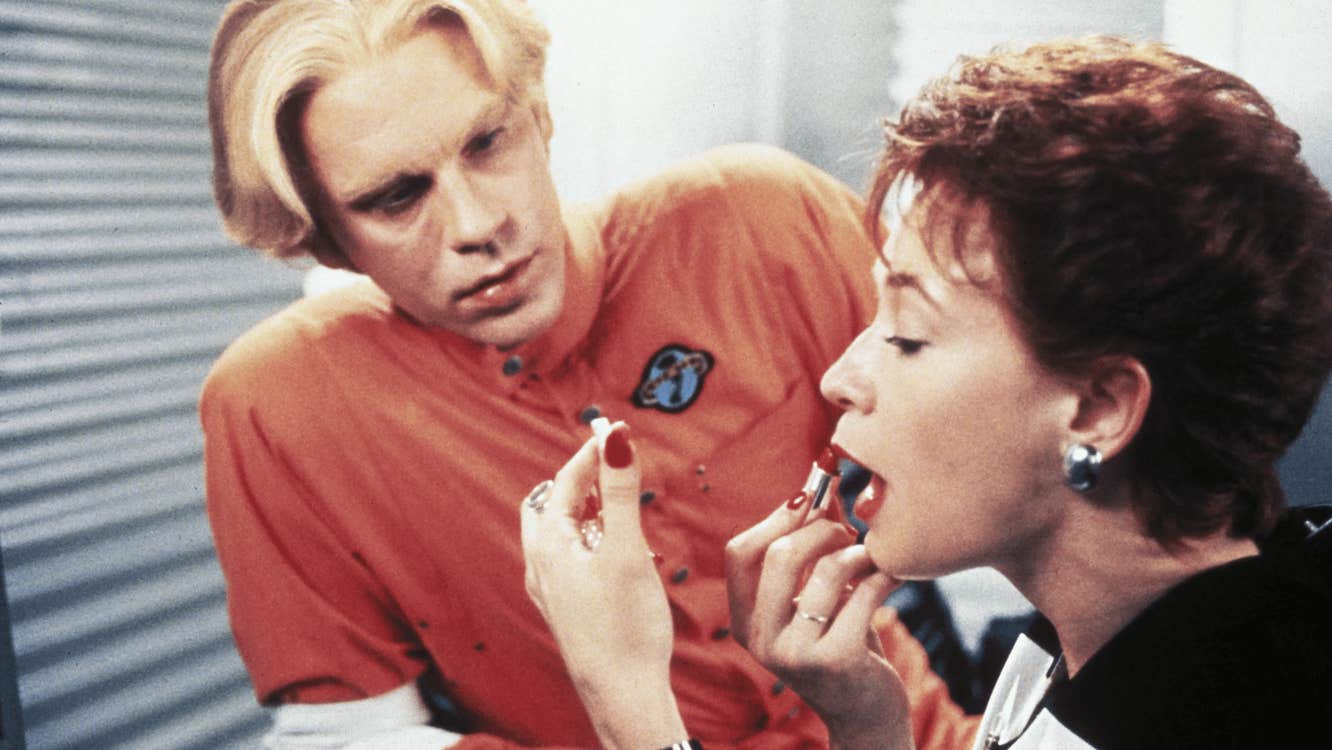 A man looking at a woman putting on lipstick.