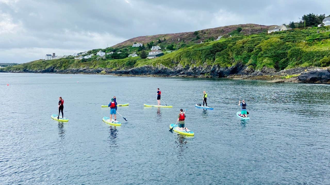 A group stand up paddle boarding along a craggy coastline