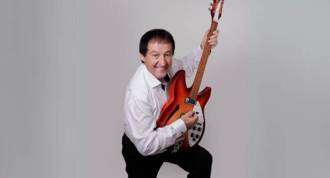 Declan Nerney live at Backstage Theatre Longford, a smiling man holding up a guitar vertically, resting on raised left knee.