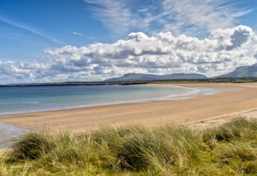 A view of a sandy beach under a blue sky with large clouds