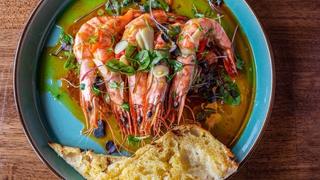 Prawns surrounded by oil on a blue plate with two slices of bread on the edge