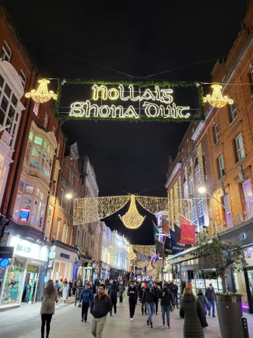 Looking down a shopping street with buildings in a street at night with yellow christmas lights across the between them.