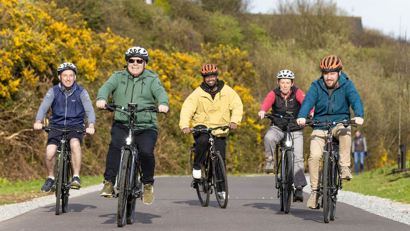 A group cycling on a country road with colourful bushes in the background