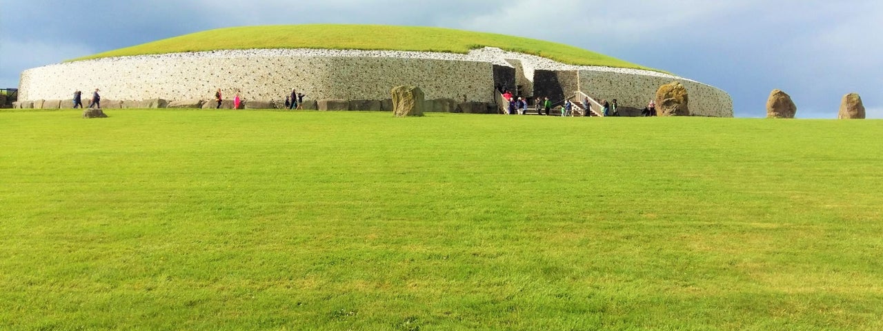 An image of Newgrange with green grass in foreground and a backdrop of a moody grey sky