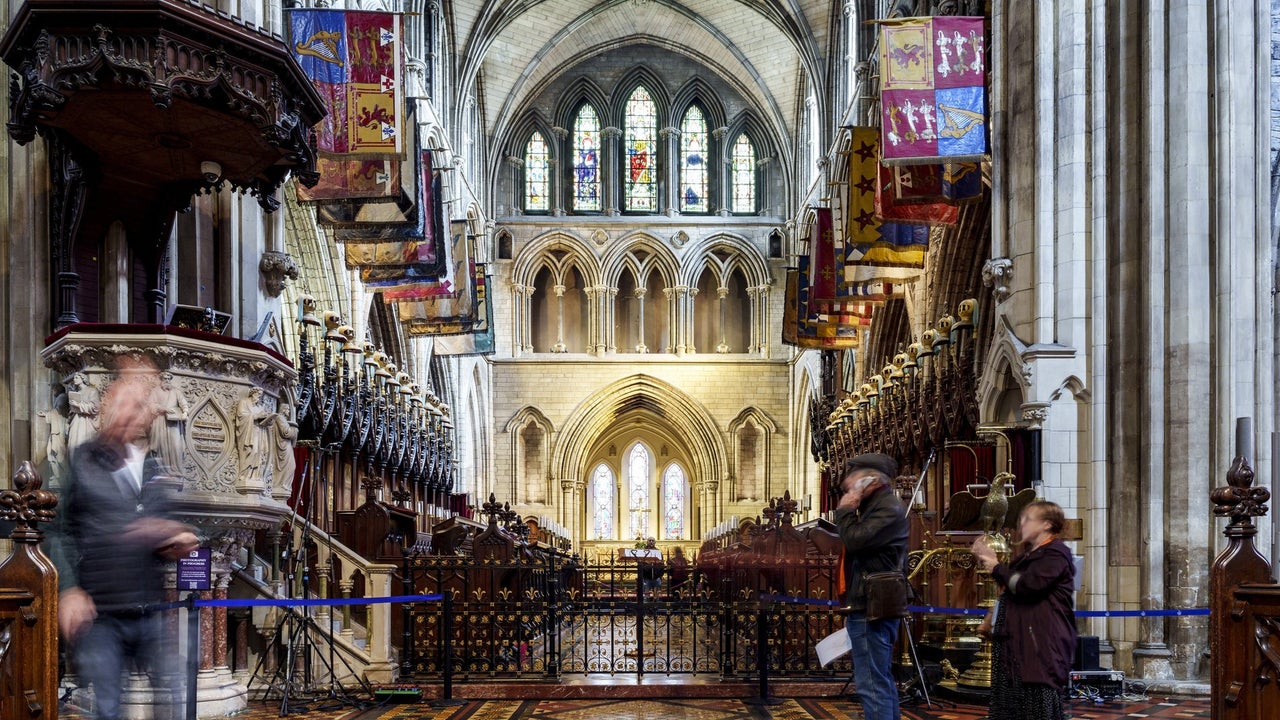 Nave of a church with banners on either side and stain glass windows in the background