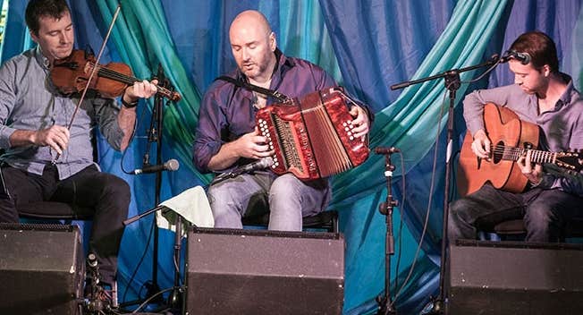 Joyce Brothers Music Festival 2026, 3 seated musicians playing instruments on a small stage area.