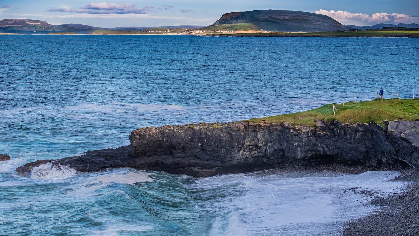 A person standing on Aughris Head, Sligo with a mountain in the background.