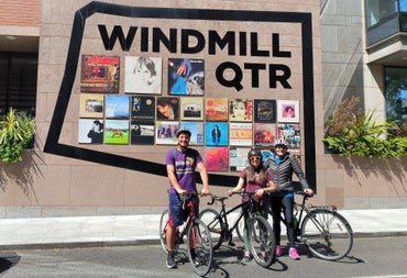 Three people on bikes outside a building with album covers displayed on it