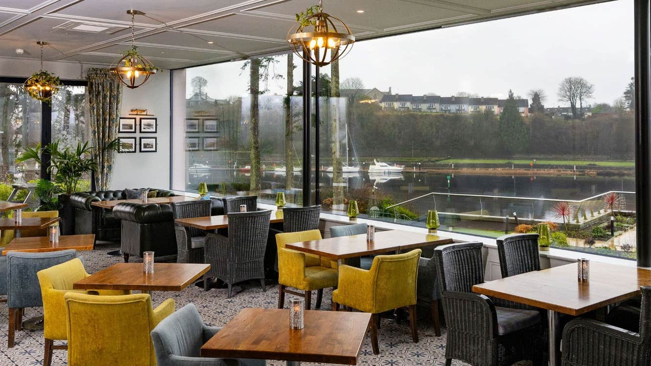 Interior of a restaurant with tables grey and yellow chairs and a window overlooking water