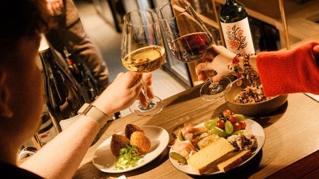 Table with plates of food and two people each holding a wine glass