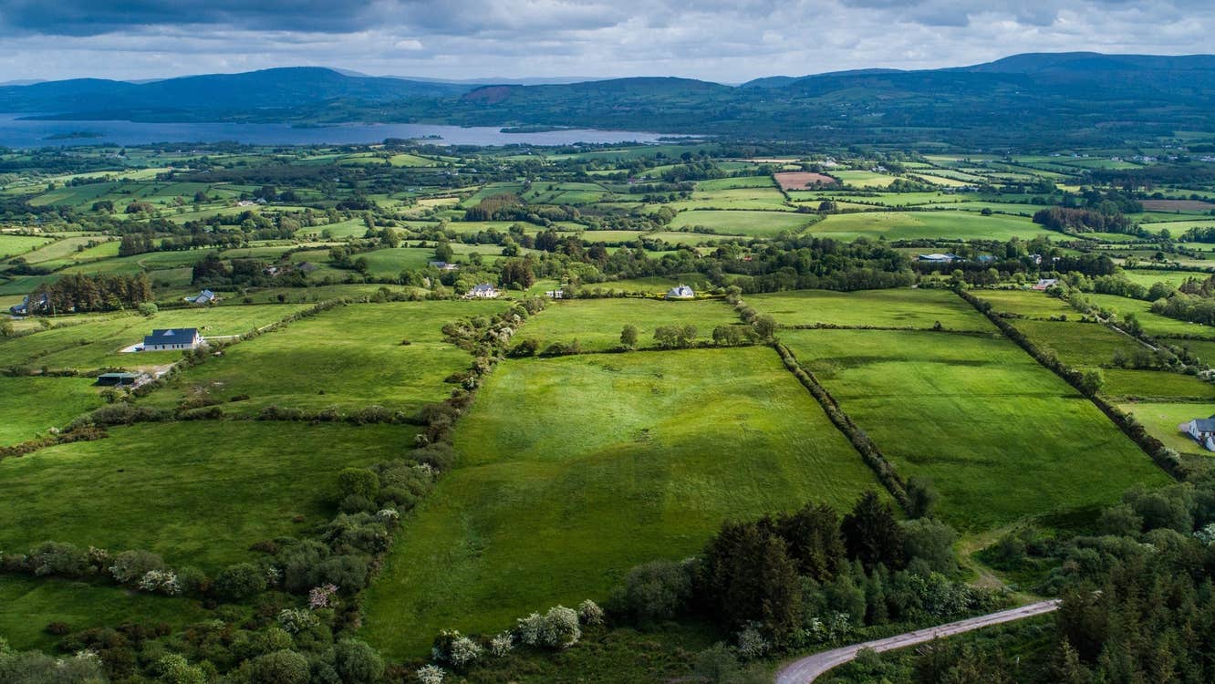 Aerial view of green fields a lake and mountains with a cloudy sky
