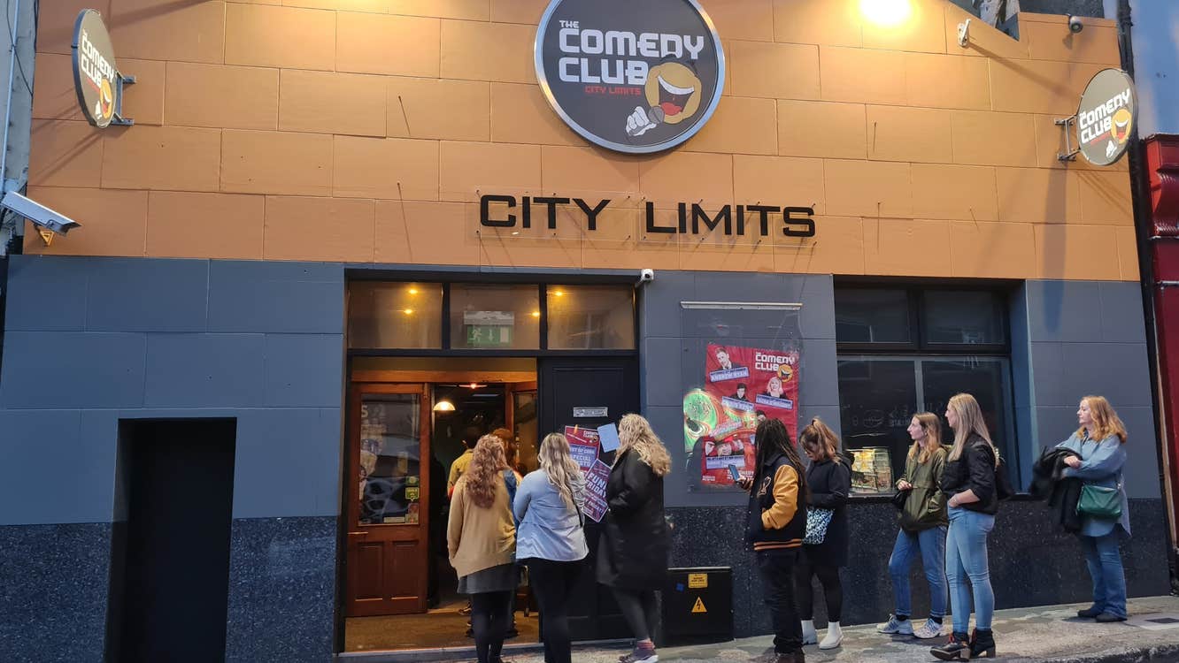 People waiting outside a grey and yellow building.