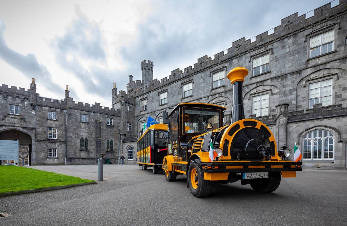 A black and yellow coloured tourist train parked in courtyard of Kilkenny Castle