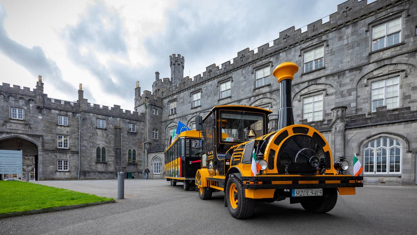 A black and yellow coloured tourist train parked in courtyard of Kilkenny Castle