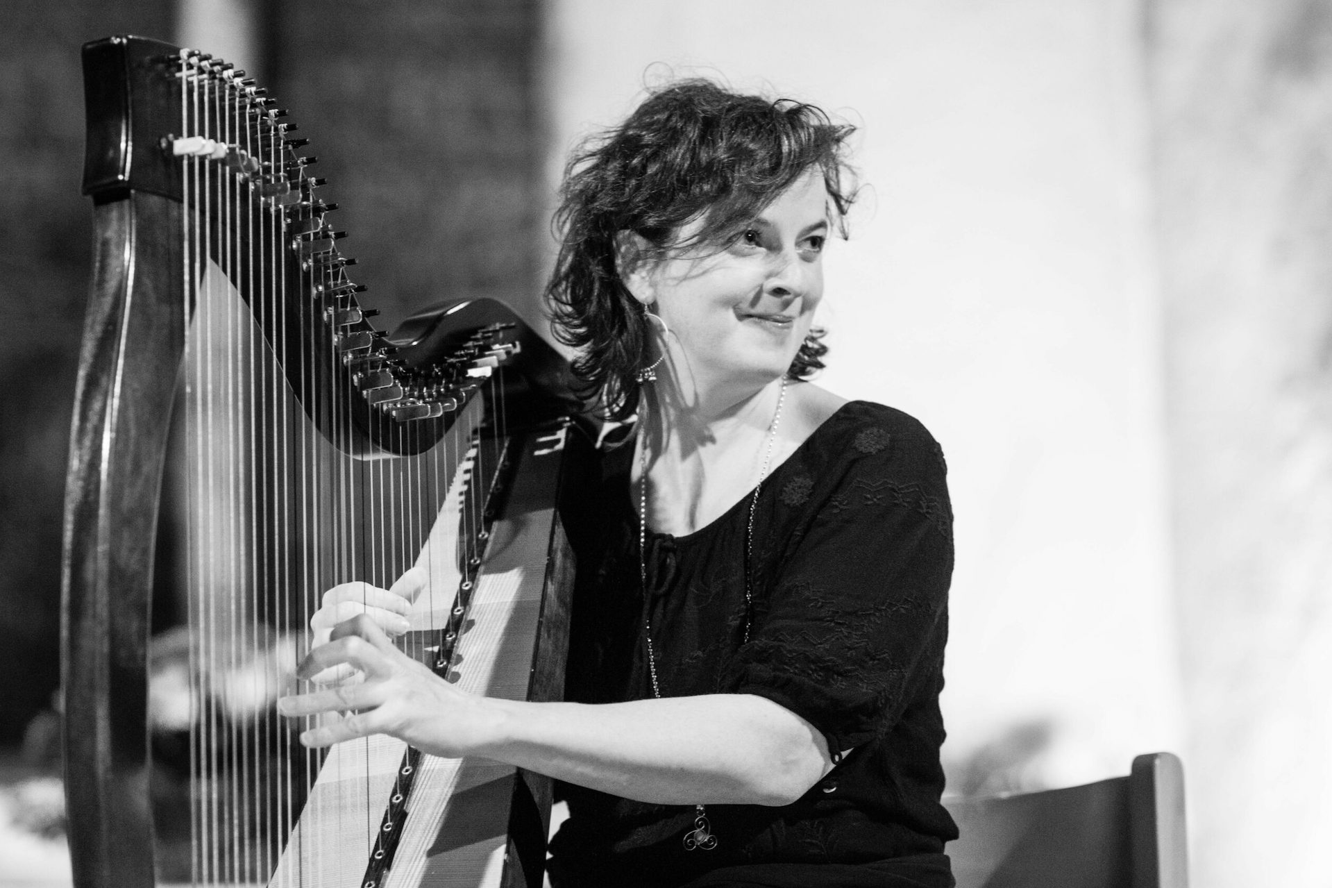 Black and white image of woman smiling, looking away to her left, playing a large harp.