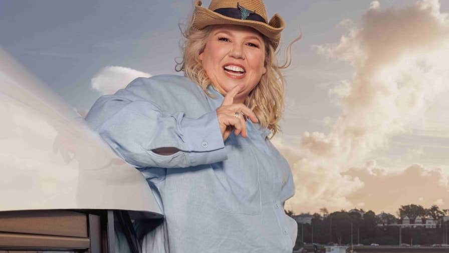 A laughing woman wearing a brown cowboy style hat outdoors with harbour in background.