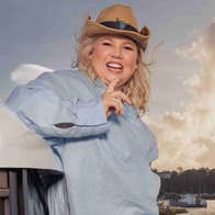 A laughing woman wearing a brown cowboy style hat outdoors with harbour in background.