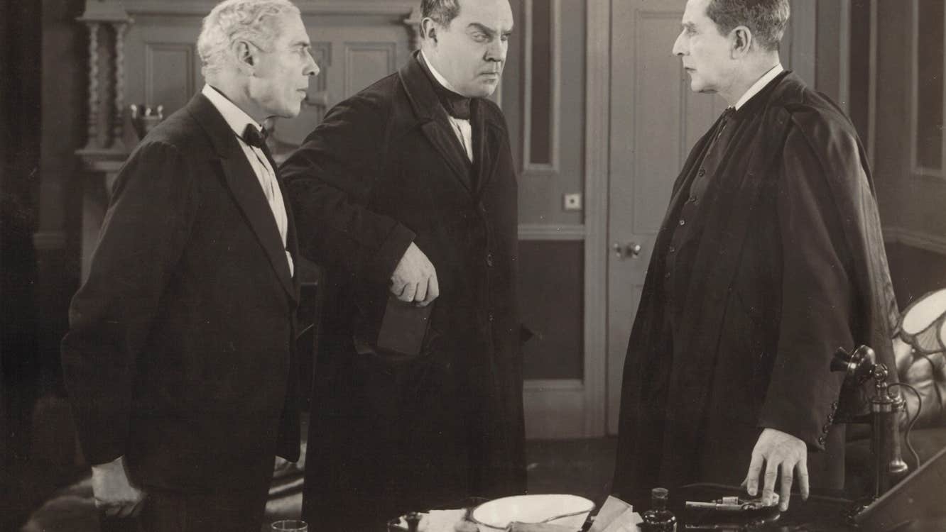 Three men in 19th century clothing are talking in a room.