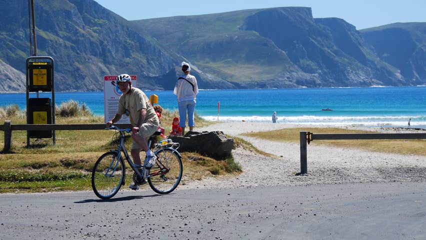 A cyclist at an entrance to a beach with mountains in the background