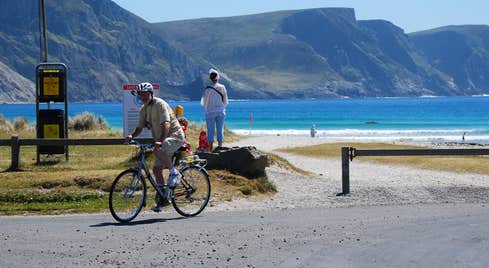 A cyclist at an entrance to a beach with mountains in the background