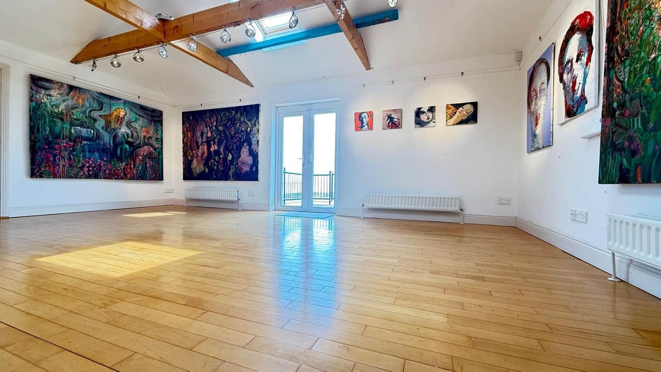 A large room with wooden flooring and white walls with artworks on display