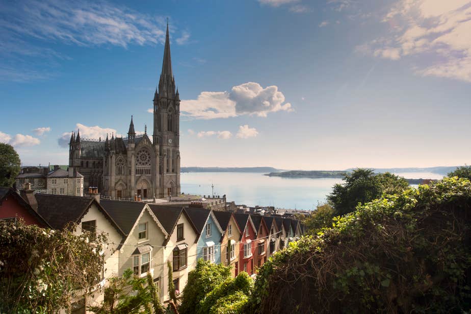 A row of colourful houses with St Colman's Cathedral in the background in Cobh, County Cork