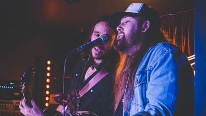 Walker Tex & Wilson Lyons playing guitars and singing into the one mic on a stand.