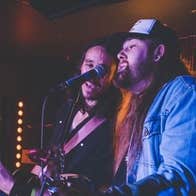 Walker Tex & Wilson Lyons playing guitars and singing into the one mic on a stand.