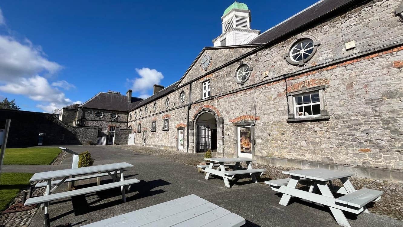 Four picnic benches on a paved area outside a big stone building