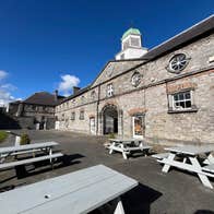 Four picnic benches on a paved area outside a big stone building