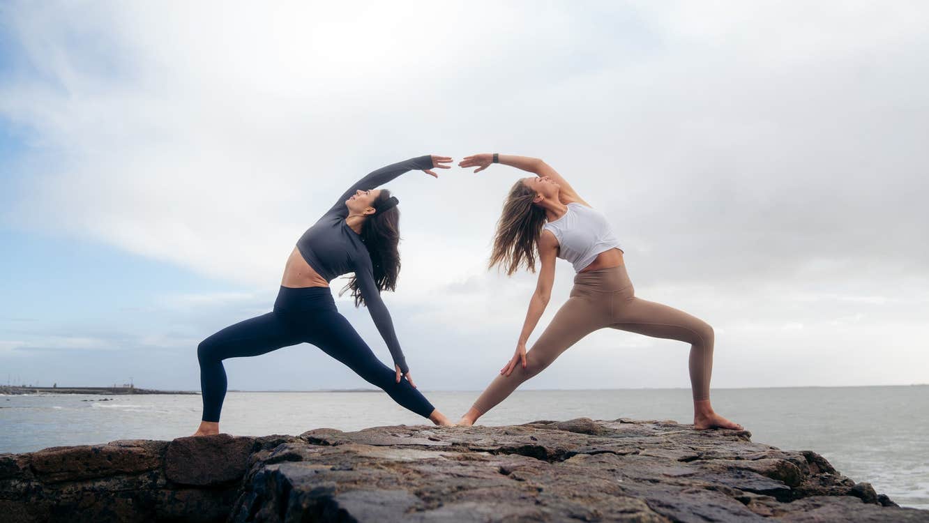 Two people doing yoga stretches on rocks next to the sea