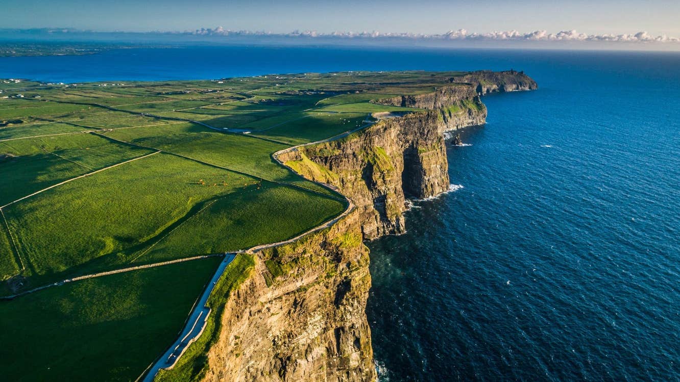 Steep coastal sea cliffs overlook the Atlantic Ocean bordered by green fields and walking paths