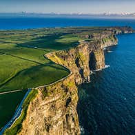 Steep coastal sea cliffs overlook the Atlantic Ocean bordered by green fields and walking paths