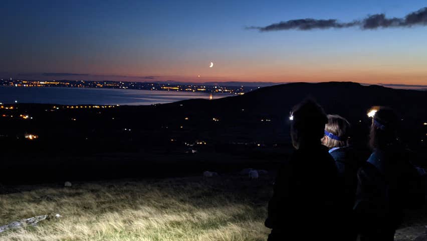 Three walkers on the Cooley Mountains at dusk overlooking the lough