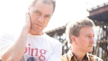 2 men outside with tall structure in background.