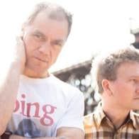2 men outside with tall structure in background.