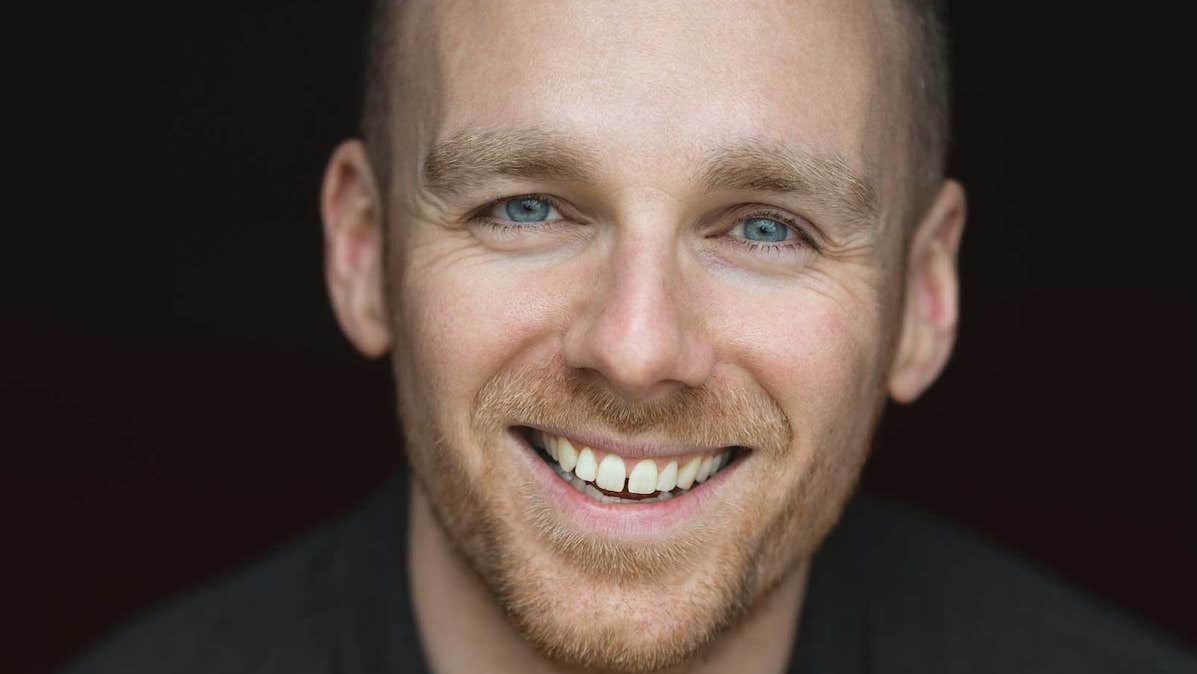 Close up view of man's face, smiling against black background.