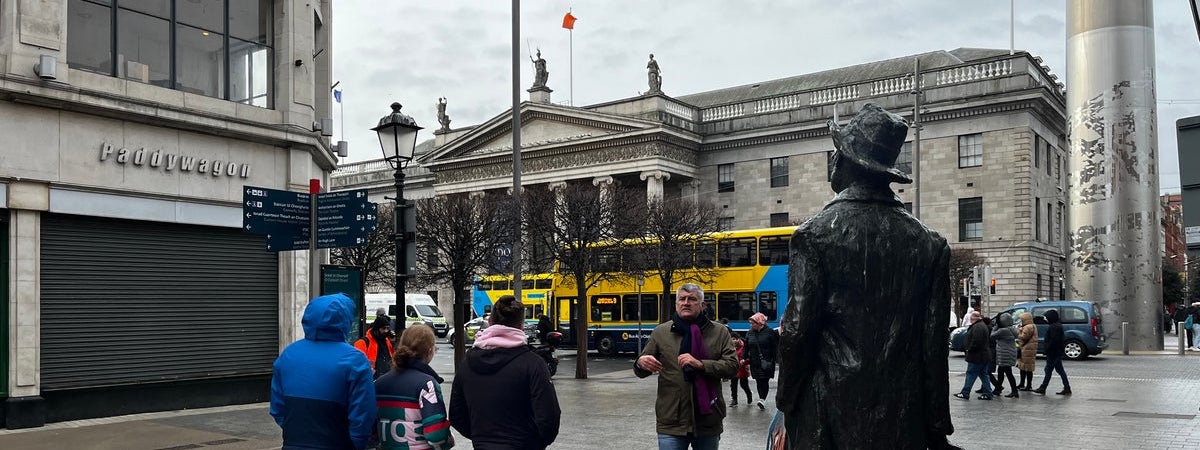 A group of people and a tour guide at a statue in Dublin