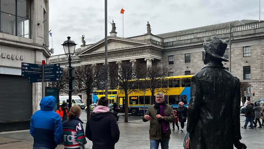A group of people and a tour guide at a statue in Dublin